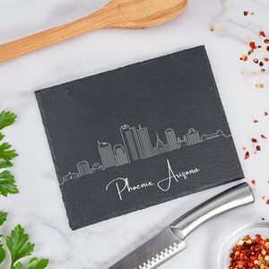 May include: Black slate serving tray with a white outline of the Phoenix, Arizona skyline and the text "Phoenix, Arizona".