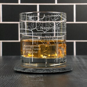 May include: A clear glass with a map of Naperville, Illinois etched on the side. The glass is filled with amber liquid and ice cubes. The text "Springbrook Prairie Forest Preserve" is visible at the bottom of the glass.