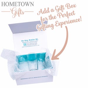 May include: A white gift box with a teal interior insert and bubble wrap, containing a clear glass. The box lid features the text HOMETOWN Gifts and Blue Ridge Mountain Gifts. Text on the box reads Add a Gift Box for the Perfect Gifting Experience!