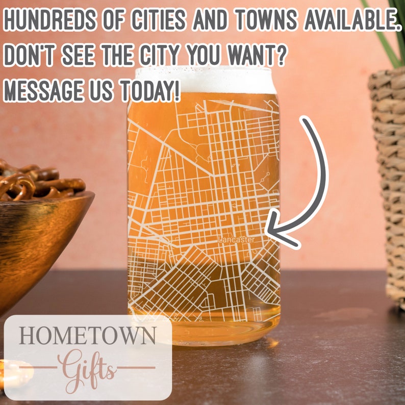 May include: A glass beer mug with an etched design of a city map. The mug is filled with a light amber liquid. The text "Lancaster" is visible on the map. The text "HOMETOWN -Gifts- " is visible at the bottom of the image.
