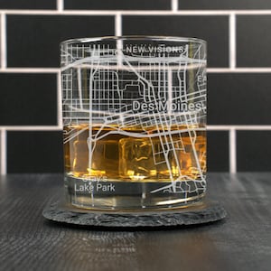 May include: A clear glass with a design of the Des Moines, Iowa city map etched on the side. The glass is filled with amber liquid and ice cubes. The text "Gray's Lake Park" is visible at the bottom of the glass.