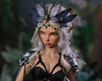 May include: A doll with white hair wearing a black bra and a skirt with a silver skull and chain detail. The doll is wearing a crown with butterfly wings and a green gem.