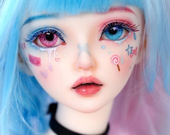 Puede incluir: Primer plano del rostro de una muñeca con cabello azul y rosa. Un ojo es rosa, el otro azul, con maquillaje a juego. La muñeca tiene lágrimas y decoraciones en las mejillas pintadas, y lleva un choker negro.
