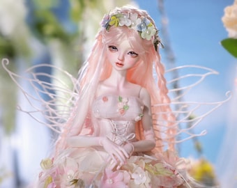 May include: A detailed doll with long, pink hair and a floral crown. The doll is dressed in a light pink gown decorated with flowers and has delicate, white, wing-like structures. The doll's face is painted with soft features.