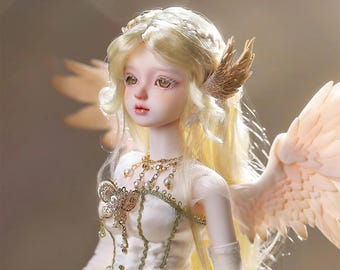 May include: A detailed doll with a serene expression, blonde hair, and delicate features. The doll wears a white dress with gold accents, a butterfly-shaped pendant, and feathered wings. The doll has a gold wing on the side of its head.