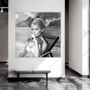 Puede incluir: Impresi&oacute;n art&iacute;stica en blanco y negro de una mujer en bikini bebiendo de un vaso. La imagen est&aacute; ambientada en una playa con monta&ntilde;as y un pueblo costero al fondo. La mujer est&aacute; sentada en una tumbona.