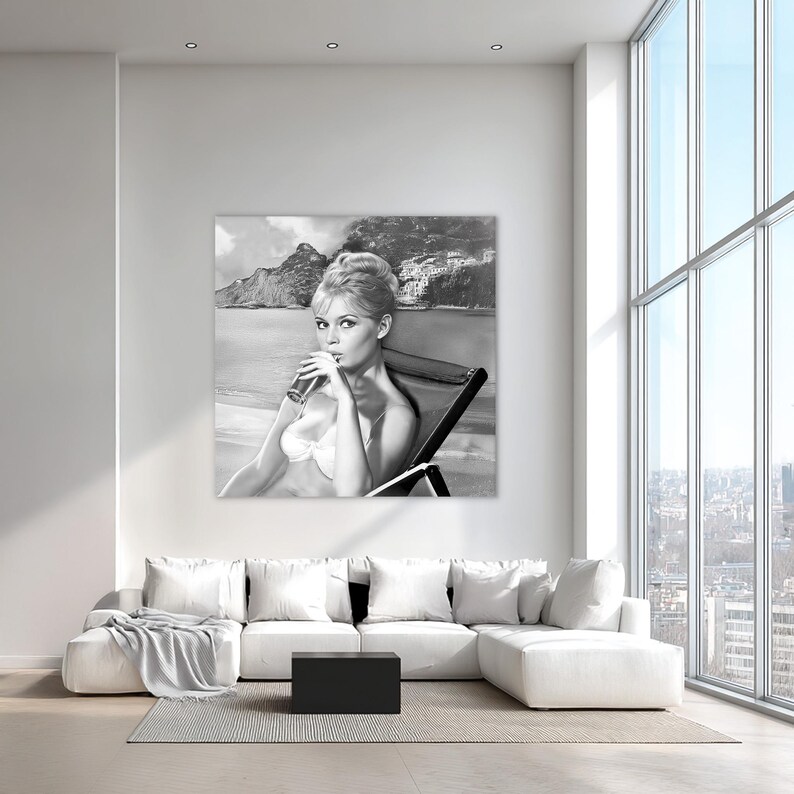 Puede incluir: Fotograf&iacute;a en blanco y negro de una mujer en bikini bebiendo de un vaso. Est&aacute; sentada en una silla de playa con un fondo esc&eacute;nico de monta&ntilde;as y un pueblo costero. La imagen es una impresi&oacute;n de estilo vintage.