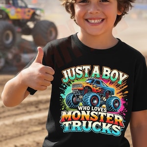 May include: A young person wearing a black t-shirt with the text "JUST A BOY WHO LOVES MONSTER TRUCKS" and a graphic of a monster truck. In the background, a monster truck crushes cars at a dirt track.