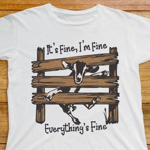 May include: White t-shirt with a brown wooden fence and a goat sticking its head through the fence. The text "It's Fine, I'm Fine Everything's Fine" is printed on the shirt.