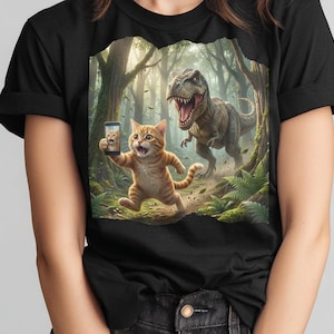 May include: Black t-shirt featuring a whimsical illustration of an orange tabby cat taking a selfie with a smartphone while running from a Tyrannosaurus Rex in a forest setting. The cat's selfie shows its face. The background includes trees and ferns.