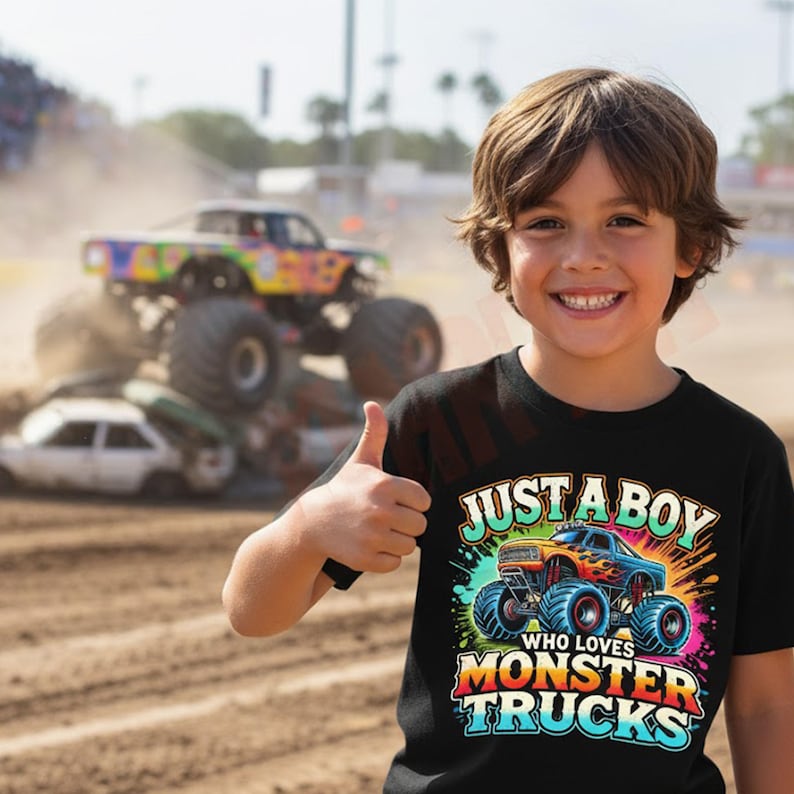 May include: A young person wearing a black t-shirt with the text "JUST A BOY WHO LOVES MONSTER TRUCKS" and a graphic of a monster truck. In the background, a monster truck crushes cars at a dirt track.