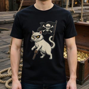Puede incluir: Camiseta negra con un gato pirata de dibujos animados. El gato lleva un parche en el ojo y sostiene una espada de madera y una bandera pirata con una calavera y huesos cruzados. Un diseño caprichoso con temática pirata.