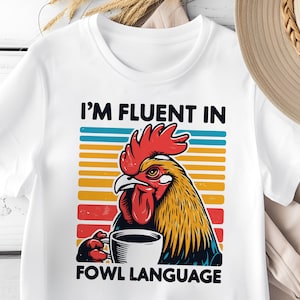 Könnte beinhalten: Weißes T-Shirt mit einer Retro-Grafik eines Hahns, der eine Tasse Kaffee hält. Der Text "Ich spreche fließend Geflügelsprache" ist unter dem Hahn gedruckt.