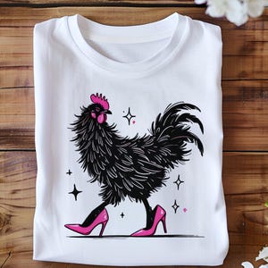 Könnte beinhalten: Weißes T-Shirt mit einem schwarzen Hahn, der rosa High Heels trägt. Der Hahn ist im Cartoon-Stil mit einem rosa Kamm und Kehllappen illustriert.