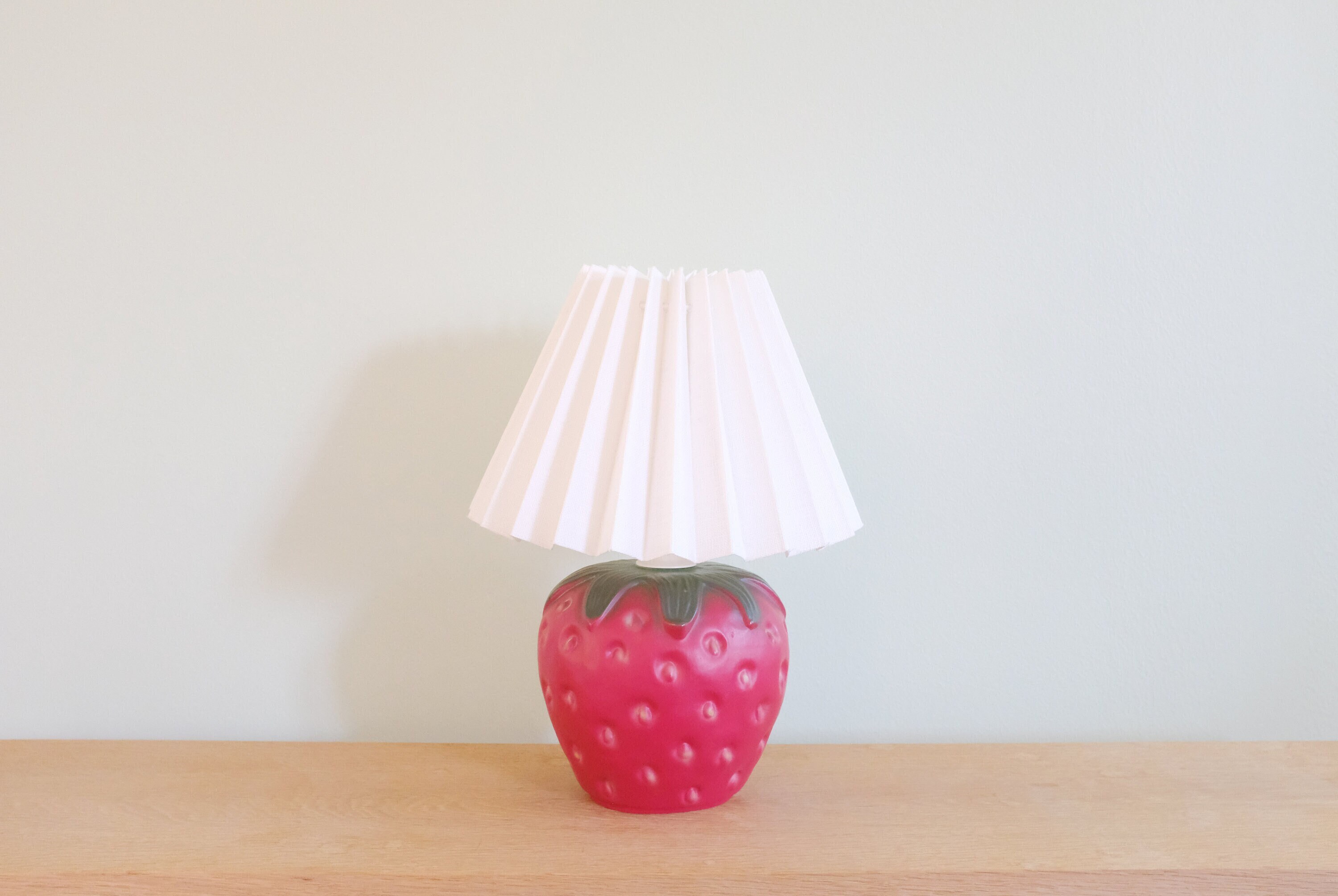 A Vintage Ceramic Strawberry Lamp With a White Fabric Pleated