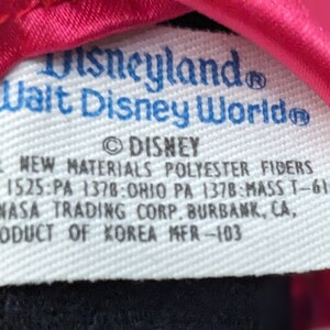 May include: White tag with blue text that reads "Disneyland Walt Disney World" and "DISNEY". The tag also includes the text "ALL NEW MATERIALS POLYESTER FIBERS ME 1525:PA 1378:OHIO PA 1378:MASS T-616 CANASA TRADING CORP. BURBANK, CA, PRODUCT OF KOREA MFR-103".