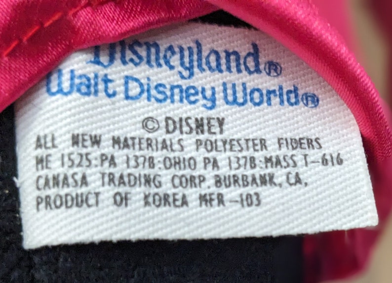 May include: White tag with blue text that reads "Disneyland Walt Disney World" and "DISNEY". The tag also includes the text "ALL NEW MATERIALS POLYESTER FIBERS ME 1525:PA 1378:OHIO PA 1378:MASS T-616 CANASA TRADING CORP. BURBANK, CA, PRODUCT OF KOREA MFR-103".