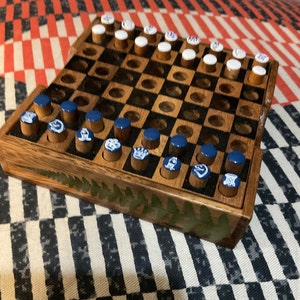 May include: A wooden checkerboard game with blue and white playing pieces. The board has a dark wood finish and a green fern design painted on the side.