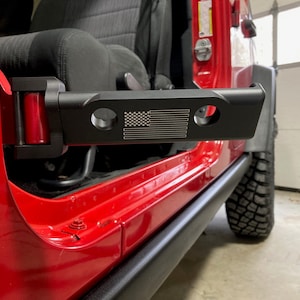 May include: A red Jeep Wrangler with a black door handle that has an American flag design etched into it.