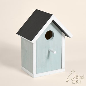 K&ouml;nnte beinhalten: Ein hellblaues Vogelhaus mit schwarzem Dach und wei&szlig;en Verzierungen. Das Vogelhaus hat ein rundes Eingangsloch und einen kleinen Sitzplatz.