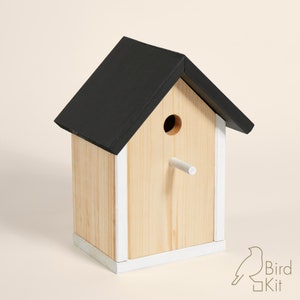 K&ouml;nnte beinhalten: Ein Vogelhaus aus Holz mit einem schwarzen Dach und wei&szlig;en Verzierungen. Das Vogelhaus hat ein rundes Eingangsloch und einen kleinen Sitzplatz.