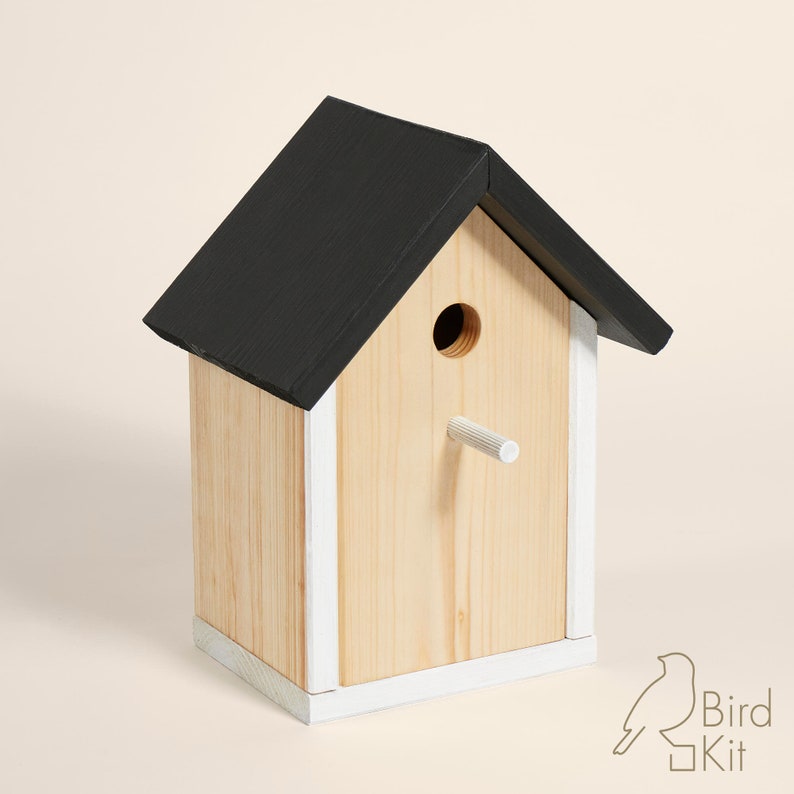 K&ouml;nnte beinhalten: Ein Vogelhaus aus Holz mit einem schwarzen Dach und wei&szlig;en Verzierungen. Das Vogelhaus hat ein rundes Eingangsloch und einen kleinen Sitzplatz.
