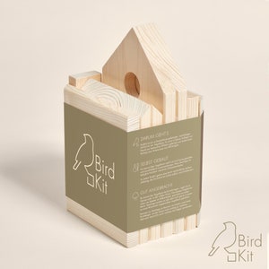 K&ouml;nnte beinhalten: Ein Vogelhaus-Set aus Holz mit Anleitung auf der Seite. Das Set besteht aus Naturholz und ist montagefertig. Die Anleitung enth&auml;lt Informationen &uuml;ber die Bedeutung von Vogelh&auml;usern und deren Bau. Das Set hei&szlig;t "Bird Kit" und zeigt ein Vogel-Logo.