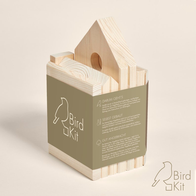 K&ouml;nnte beinhalten: Ein Vogelhaus-Set aus Holz mit Anleitung auf der Seite. Das Set besteht aus Naturholz und ist montagefertig. Die Anleitung enth&auml;lt Informationen &uuml;ber die Bedeutung von Vogelh&auml;usern und deren Bau. Das Set hei&szlig;t "Bird Kit" und zeigt ein Vogel-Logo.