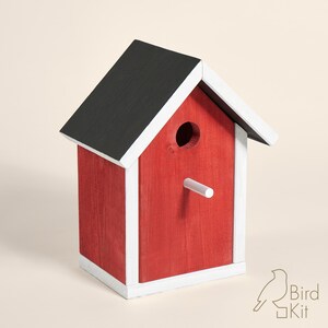 K&ouml;nnte beinhalten: Rotes Vogelhaus aus Holz mit schwarzem Dach und wei&szlig;em Rahmen. Das Vogelhaus hat ein rundes Eingangsloch und einen kleinen Sitzplatz.