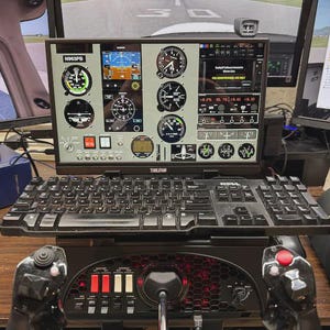 May include: A flight simulator setup featuring a central monitor displaying a digital aircraft cockpit dashboard with various gauges, a black Dell keyboard, and a black control yoke with red and black buttons positioned in the foreground.