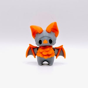 May include: A small, gray, 3D printed bat figurine with orange wings and a fuzzy orange body.