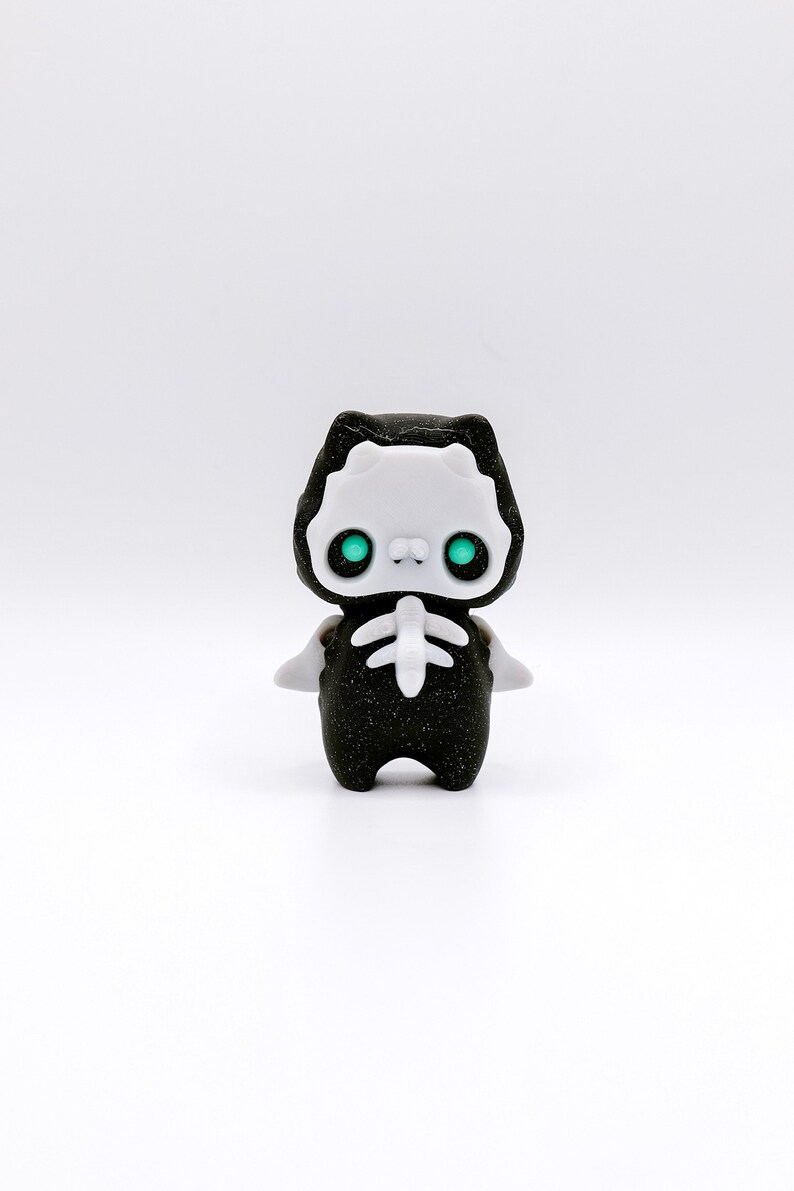 May include: A small black and white figurine of a cat wearing a skeleton costume. The cat has green eyes and a sparkly black body.