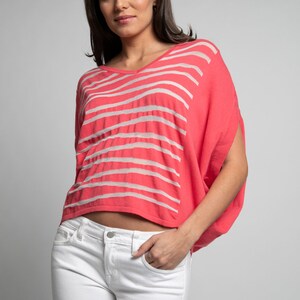 Puede incluir: Una mujer lleva una camisa de rayas rosa y blancas con un corte holgado y un dobladillo recortado. Tambi&eacute;n lleva pantalones vaqueros blancos.