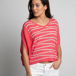 Puede incluir: Una mujer con una camisa de manga corta a rayas rosa y blancas con cuello en V y pantalones vaqueros blancos.