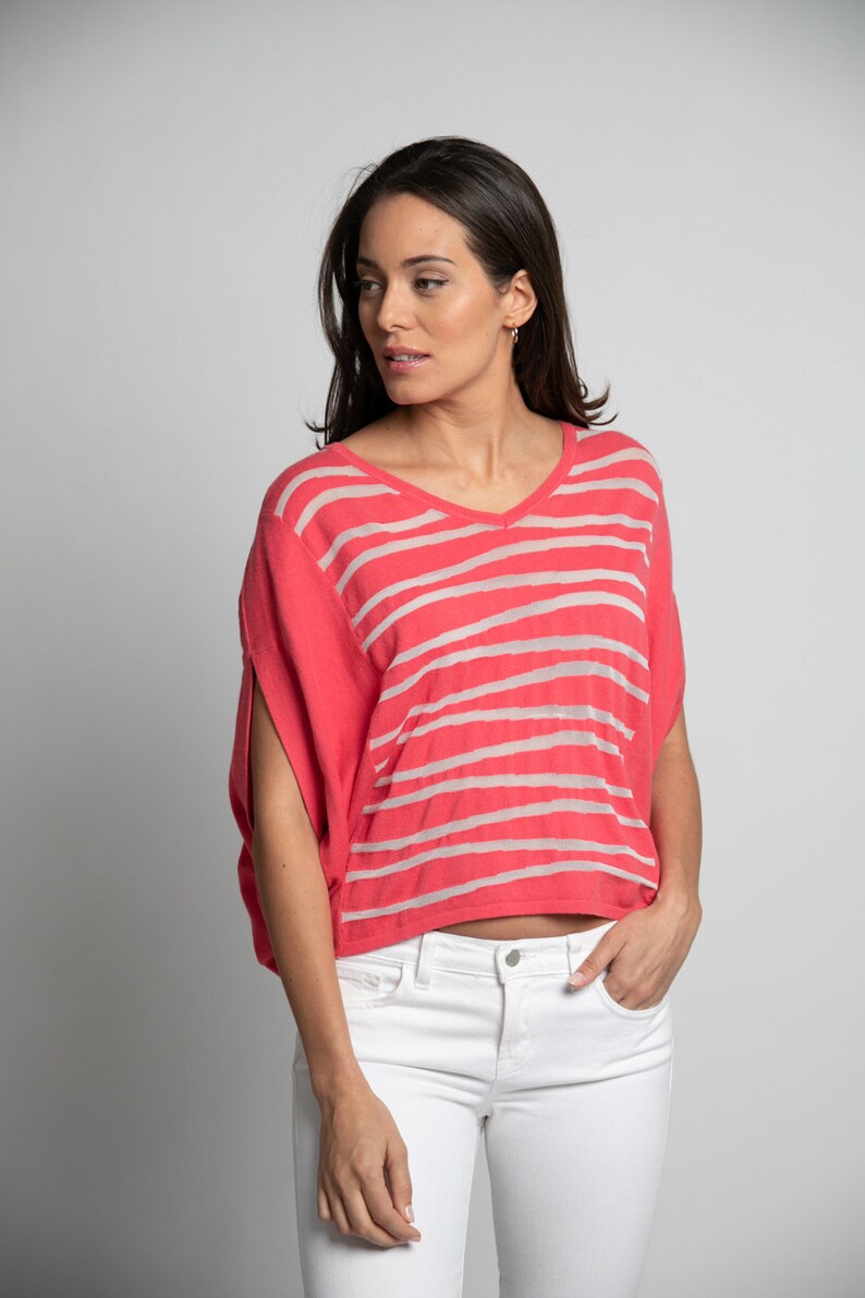 Puede incluir: Una mujer con una camisa de manga corta a rayas rosa y blancas con cuello en V y pantalones vaqueros blancos.