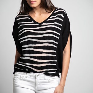 Pode incluir: Uma mulher vestindo uma camisa listrada preta e branca com decote em V e calças jeans brancas.