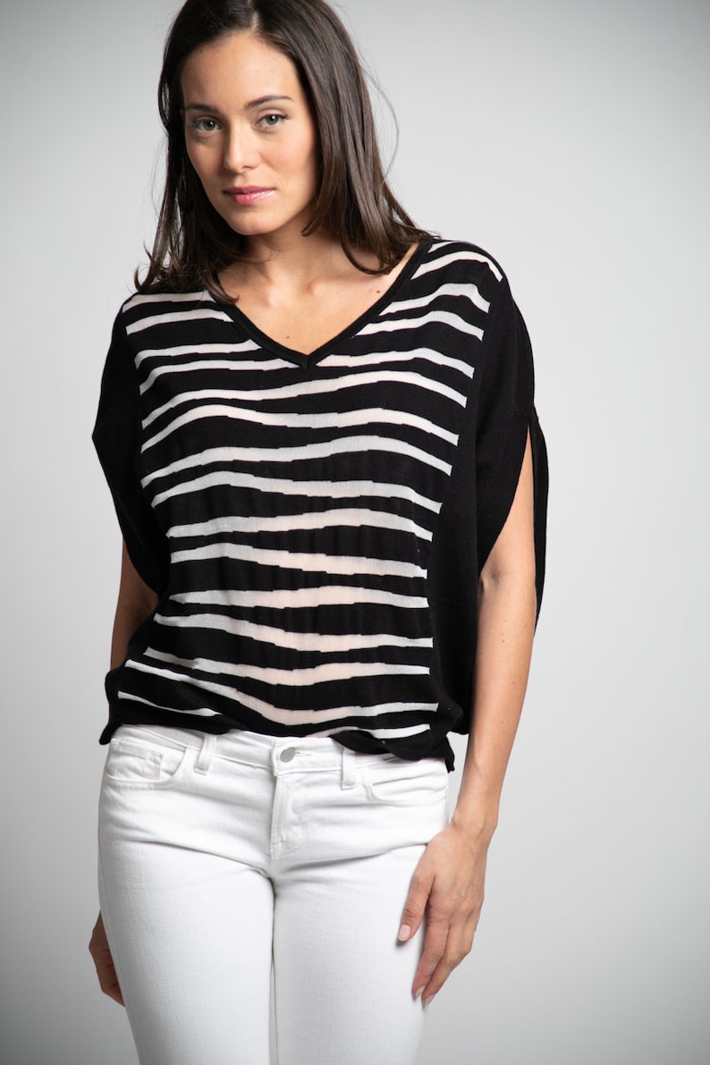 Puede incluir: Una mujer con una camisa de rayas blancas y negras con cuello en V y pantalones vaqueros blancos.