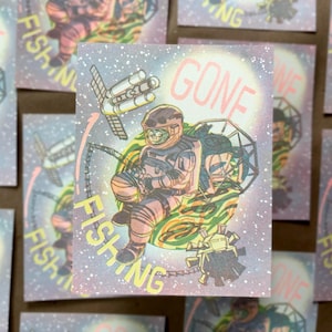 May include: A rectangular sticker featuring a space-themed illustration of an astronaut sitting on a green planet, holding a fishing rod. A satellite and space debris float nearby. The text GONE FISHING is printed in yellow and pink letters.