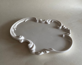 Puede incluir: Bandeja de cerámica blanca con un borde decorativo, ornamentado y festoneado.