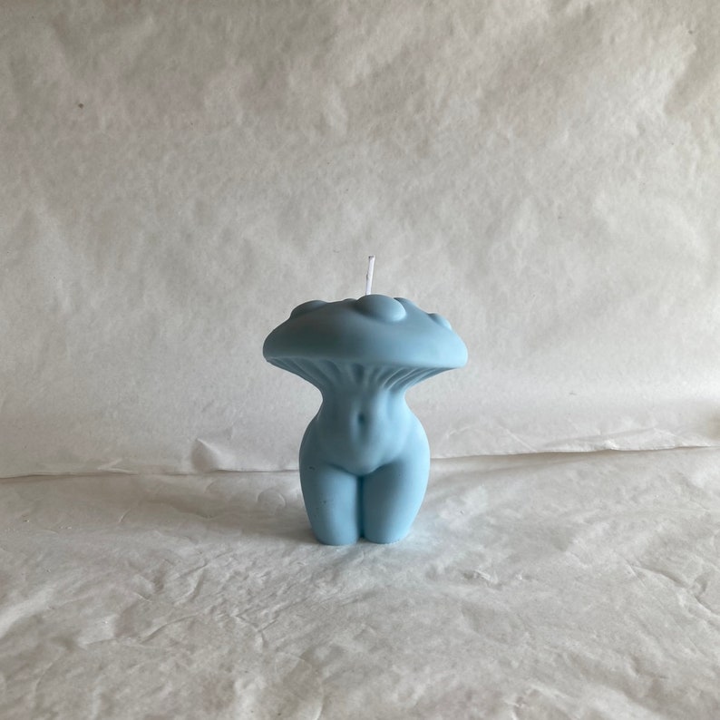 K&ouml;nnte beinhalten: Eine hellblaue Kerze in Form einer menschlichen Figur mit einem pilzf&ouml;rmigen Oberteil. Die Kerze hat einen wei&szlig;en Docht.