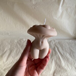 K&ouml;nnte beinhalten: Eine nude-farbene Kerze in Form eines menschlichen Torsos mit einem pilzf&ouml;rmigen Oberteil. Die Kerze ist aus Sojawachs und hat einen Baumwolldocht.