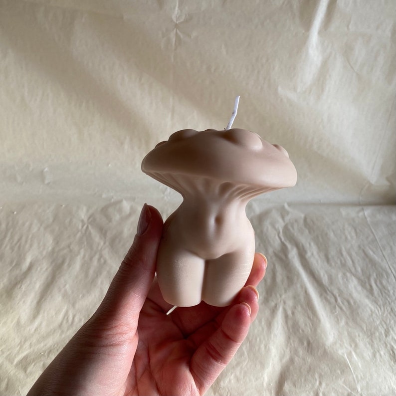 K&ouml;nnte beinhalten: Eine nude-farbene Kerze in Form eines menschlichen Torsos mit einem pilzf&ouml;rmigen Oberteil. Die Kerze ist aus Sojawachs und hat einen Baumwolldocht.