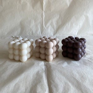 Op de afbeelding: Drie vierkante kaarsen met een uniek bubbelontwerp. De kaarsen zijn in tinten wit, beige en bruin.