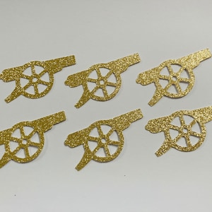 May include: Six gold glitter paper cutouts of a cannon with a wheel. The cannon is a common symbol for the Arsenal Football Club.