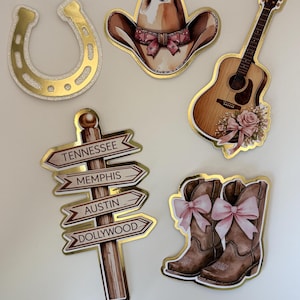 May include: A selection of country-themed die-cut stickers. Features a gold horseshoe, a cowboy hat with a pink bow, a guitar with a floral accent, a signpost with city names, and cowboy boots with pink bows.