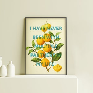 May include: A framed print with a yellow background and a green citrus branch with yellow fruit. The text "I have never been with multiple partners in my life!" is written in blue on the print.