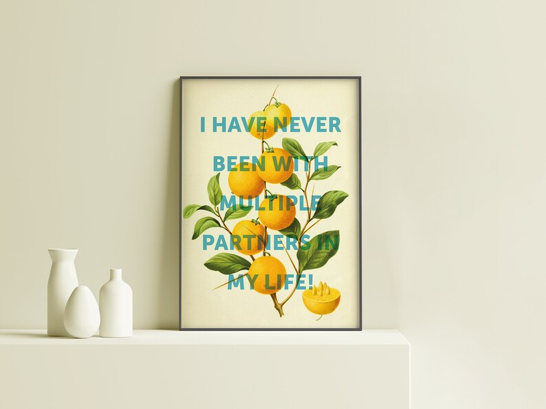 May include: A framed print with a yellow background and a green citrus branch with yellow fruit. The text "I have never been with multiple partners in my life!" is written in blue on the print.