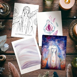 May include: Four tarot cards with watercolor and line art illustrations are arranged on a wooden surface. One card features a woman with long hair, and the text "your CRADLE of the INFINITE". Another card has the word "LUCID". Other items include feathers and candles.