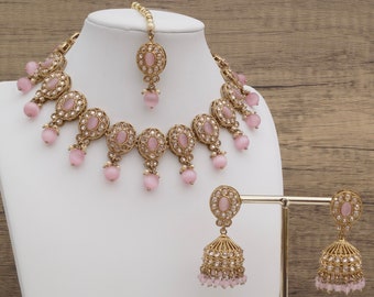 May include: A pink and gold Indian bridal jewelry set with a necklace, earrings, and a maang tikka. The necklace features pink oval stones and a gold chain with intricate details. The earrings are dangle earrings with pink stones and a gold jhumka design. The maang tikka is a small, delicate piece with a pink stone and gold chain.