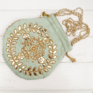 Könnte beinhalten: Eine runde, hellgrüne Kordeltasche mit goldfarbenem Blumendesign und einem Perlenkettenriemen.